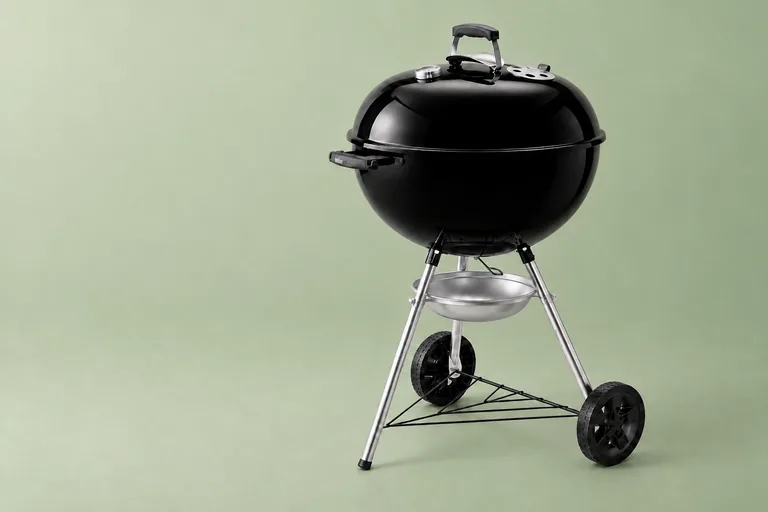 Black Weber kettle charcoal braai on a green background